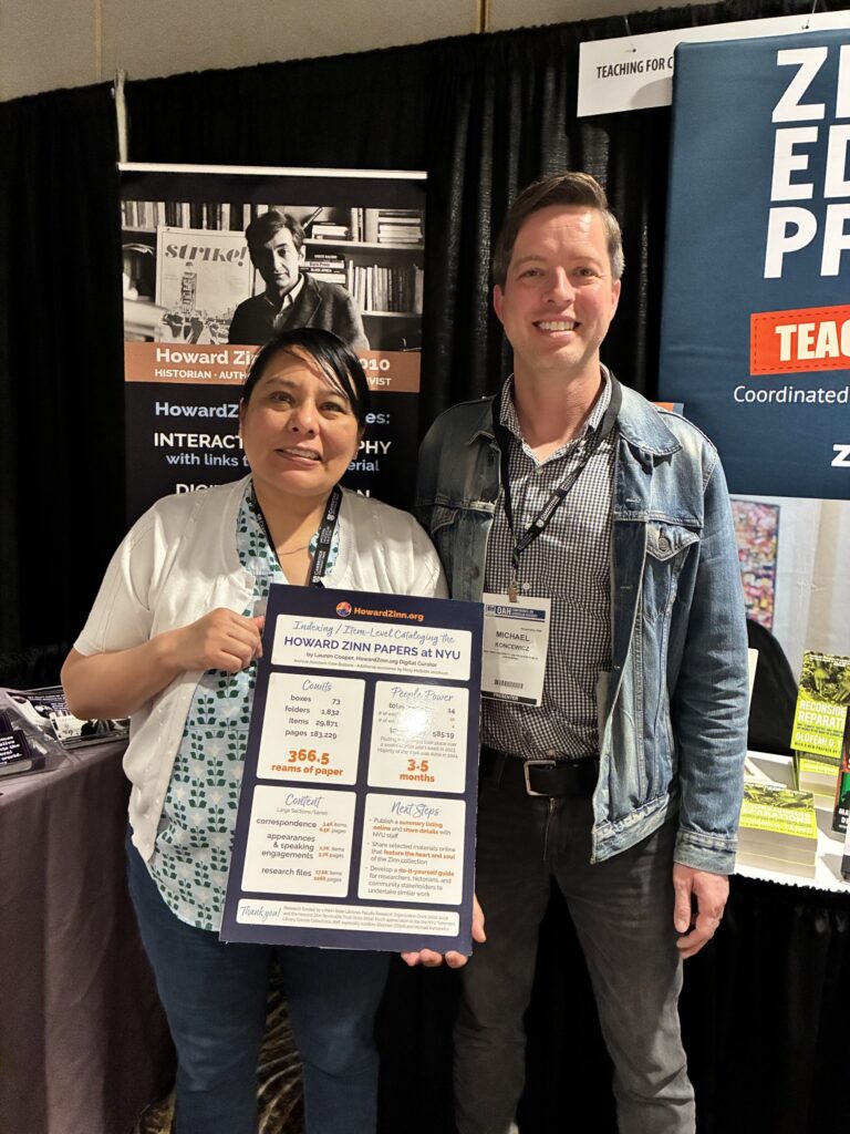 2 people in a conference booth smiling, one is holding a poster