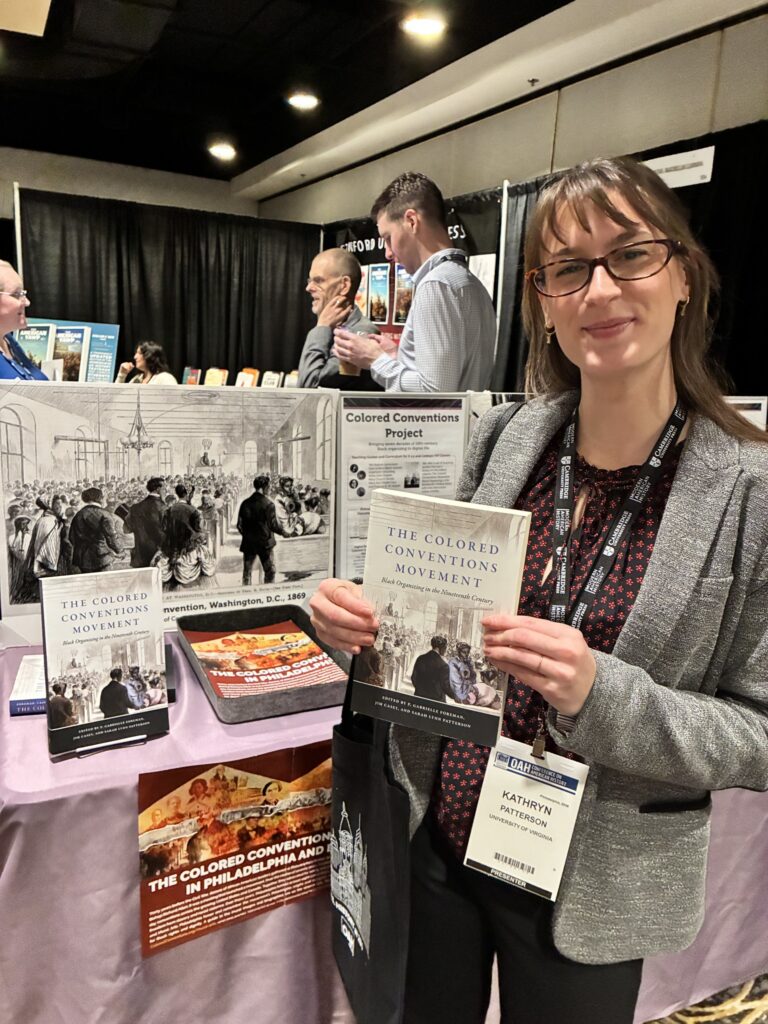 Person standing in conference booth holding a book