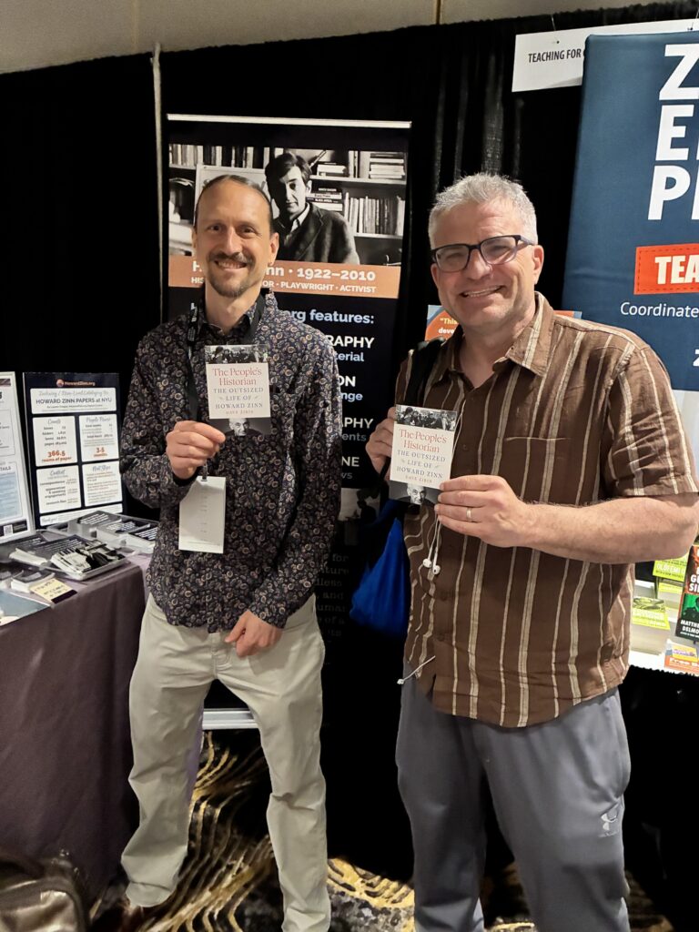 2 people smiling and holding the same book in a conference booth